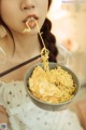 A woman holding a bowl of noodles with chopsticks in her mouth.