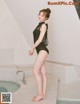 A woman in a black bathing suit standing next to a bathtub.