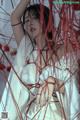 A woman in a white dress is surrounded by red strings.