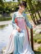 A woman in a blue and pink hanbok standing next to a body of water.