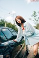 A woman leaning on the side of a black car.