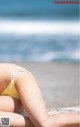 A woman in a yellow bikini sitting on the beach.