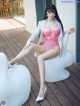 A woman in a pink lingerie sitting on a white chair.