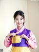 A woman in a purple and yellow hanbok holding a gold purse.