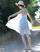 A woman in a white dress and straw hat walking down a road.