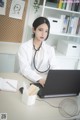 A woman in a white lab coat sitting at a desk with a laptop.