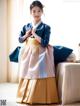 A woman in a blue and pink hanbok sitting on a bed.