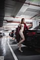 A naked woman standing next to a black car in a parking garage.