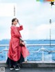 A woman in a red coat standing on a pier by the water.