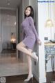 A woman in a purple dress leaning against a wall.