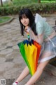 A woman sitting on a bench holding a rainbow colored umbrella.